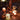 Candlelit scene with decanters, cups, and candles on a wooden surface.