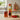 Tomato and cedarwood scent diffuser next to its container and four tomatoes on a kitchen countertop.