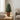 Decorative artificial cypress tree in a terracotta pot on a wooden coffee table, styled with candles, books and soft furnishings