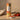 Pack of nine tea light candles on countertop next to tomatoes, with one candle lit at the front.