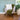 Chair with a green blanket and cream pillow in a room with a plant and window.