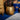 Gold textured side table next to a blue container with decorative elements on a blue rug.