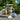 Large oxidised metal effect planter and blue and white ceramic jar on a table outdoors with greenery in the background