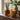 A reed diffuser bottle and a matching lit candle gift set with gold botanical patterns, on a wooden table