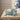 A lit square glass sea salt candle in a textured blue container with its matching lid resting beside it.
