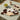 Cow print hand fan on a table with grapes, coffee, and sunglasses.