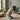 Decorative duck statue wearing a hat and green boots in a room with plants and boots.