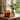 An amber glass bergamot and oud candle with a lit flame sits on a wooden table beside its lid