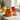 Orange glass jar next to cup and spoon on kitchen countertop, with red and yellow jars in background.