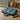 Floral-patterned dog travel bed on a stone floor with a wooden stool and basket in the background.