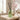 A green glass home scent diffuser bottle with black reeds sits on a light stone table in a softly lit room