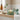 A green sakura blossom candle with a matching lid sits lit on a wooden shelf in a softly styled home setting.