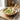 Wooden wide bowl with wood spoon and fork inside, containing salad and painted tomatoes.