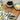 Two bowls with black olives and butter on a wooden board with a leafy background