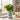 A green small artificial plant in a light blue cylindrical tin planter, placed on a kitchen counter