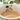 White ceramic bowl with olive design filled with a light brown liquid, blurred green leaves in the background.