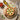 Round wooden serving board with pizza on it, surrounded by tomatoes, olive oil and a towel.