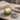 A lit two-wick floral scented candle in a textured green glass holder sits on a marble surface