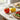 Red and yellow tomato-shaped salt and pepper shakers on white kitchen countertop next to tomatoes.