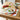 Tomatoes-painted table placemats on wooden table with plates and bread surrounded by snacks.