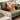 An orange pumpkin cushion sitting next to a throw blanket on a green sofa