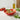 Red and green tomato-shaped kitchen bowl on white countertop with leaves, tomatoes and olive oil.