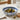 Decorative bowl with olives on a table with bread and a glass of water.